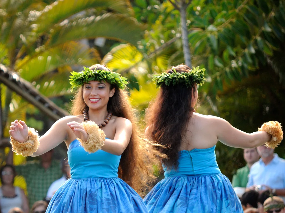 Hula tanečnice v modrých šatech vystupující na laguně během soutěže kánoí Huki ve vesnici Hawaiʻi v Polynesian Cultural Center