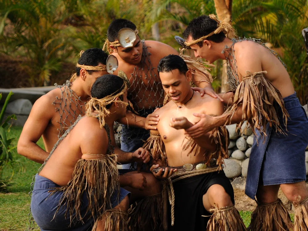 Skupina mužských umělců v tradičním tahitském oděvu shromážděná v kruhu ve vesnici Tahiti v Polynéském kulturním centru